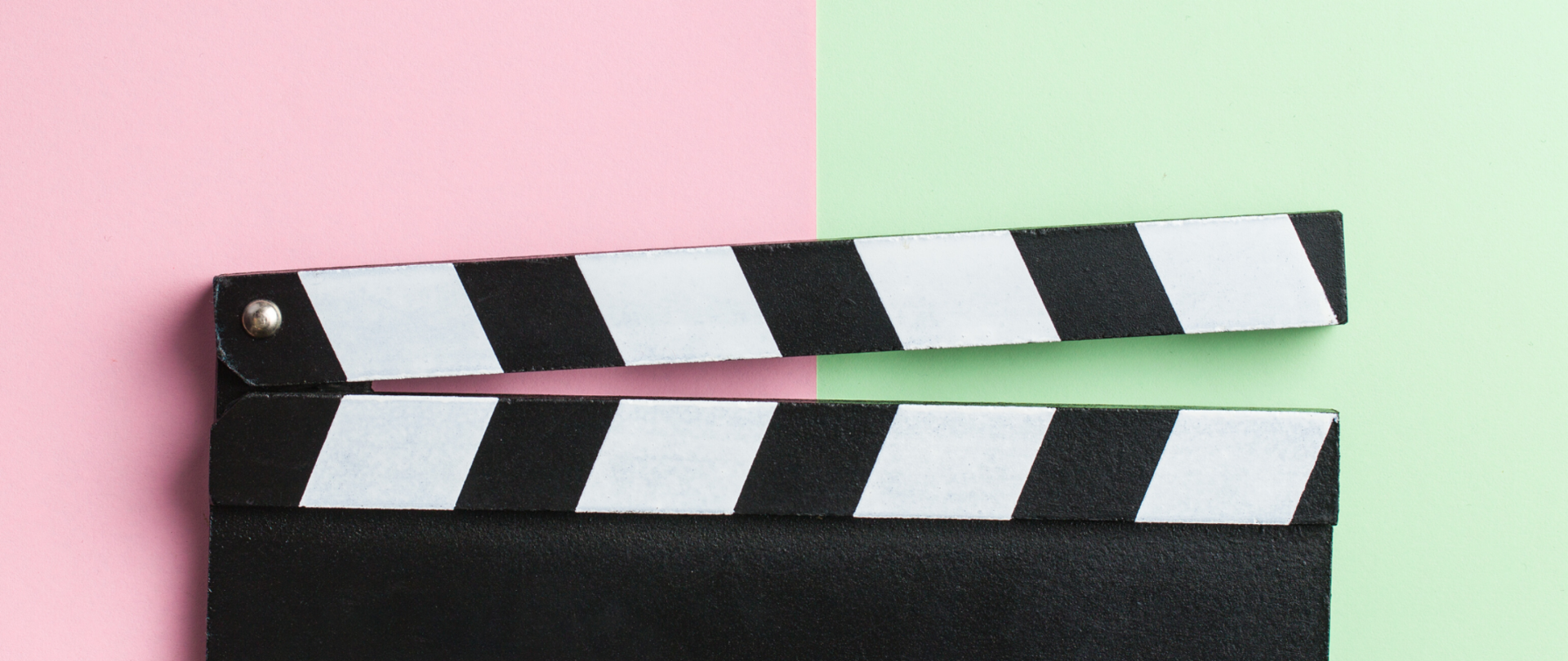 Klaps filmowy na pierwszym planie, tło podzielone na pół różowe z lewej i zielone z prawej strony.