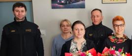 Na zdjęciu funkcjonariusze i pracownicy cywilni KP PSP w Jędrzejowie. Dwóch pracowników cywilnych trzyma w ręku okazałe bukiety kolorowych kwiatów oraz listy gratulacyjne.