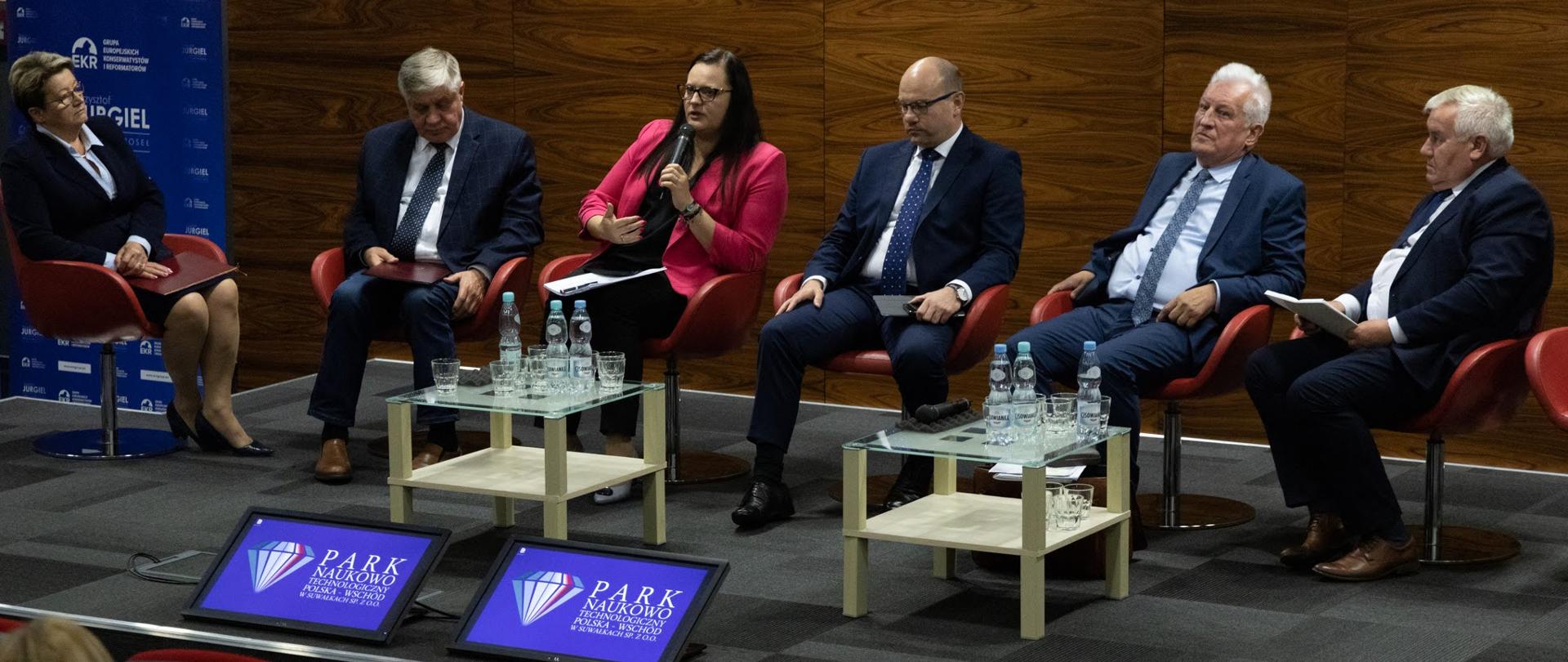 Na zdjęciu uczestnicy konferencji siedzący na fotelach, od lewej: kobieta w marynarce i spódnicy, dwóch mężczyzn w garniturach, wiceminister Małgorzata Jarosińska-Jedynak w różowej marynarce i dwóch mężczyzn. Przed siedzącymi dwa stoliki kawowe. 