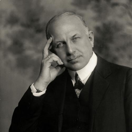 Karol Bertoni - portret mężczyzny podpierającego głowę ręką. Wąsy, siwe włosy, ciemna marynarka, musznik, ciemna kamizelka. 