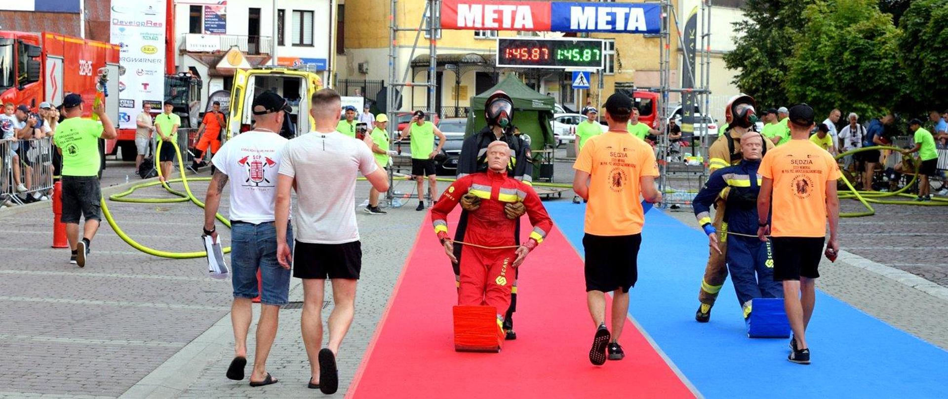 Zdjęcie zrobione na zewnątrz, na placu przy Podkarpackim Urzędzie Wojewódzkim w Rzeszowie podczas rozgrywania zawodów strażackich. Na zdjęciu strażacy wykonują konkurencje.