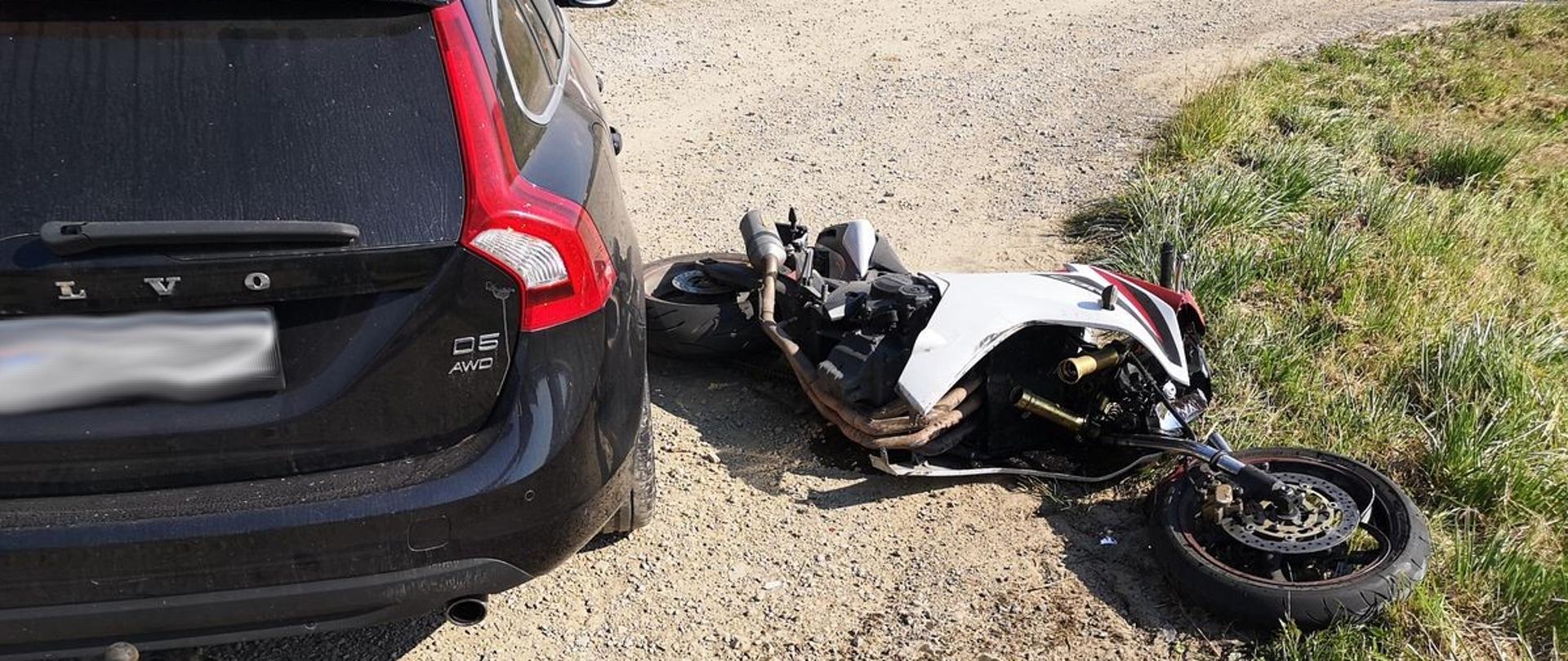 Samochód osobowy widok od tyłu a obok leży motocykl.