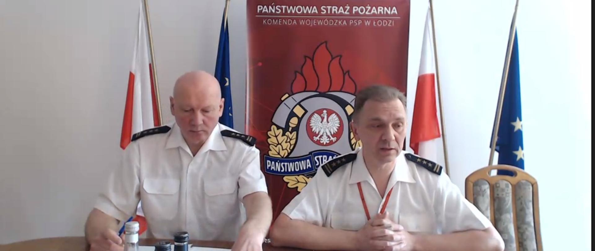 na zdjęciu widać obraz z kamery w trakcie wideokonferencji, zastępców łódzkiego Komendanta Wojewódzkiego PSP, w tle rollup Komendy Wojewódzkiej PPS w Łodzi oraz po lewej i prawej po 1 fladze Polski i unii europejskiej