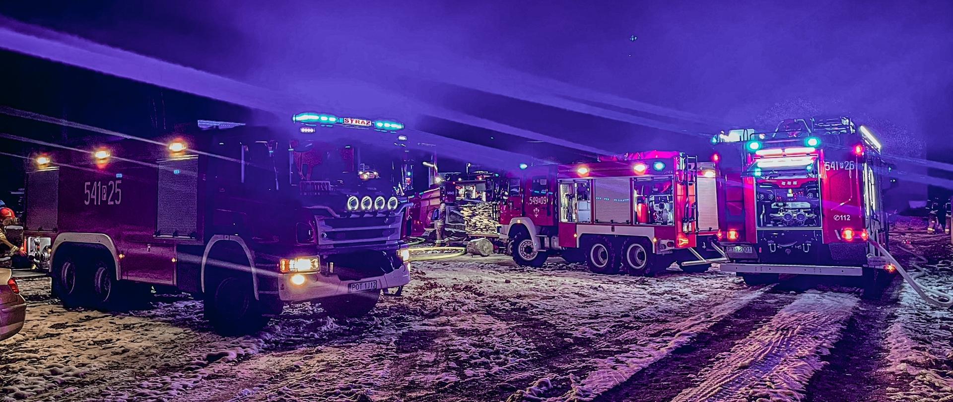Na zdjęciu trzy wozy strażackie znajdujące się przy palącym się obiekcie. Zdjęcie wykonane w porze nocnej.