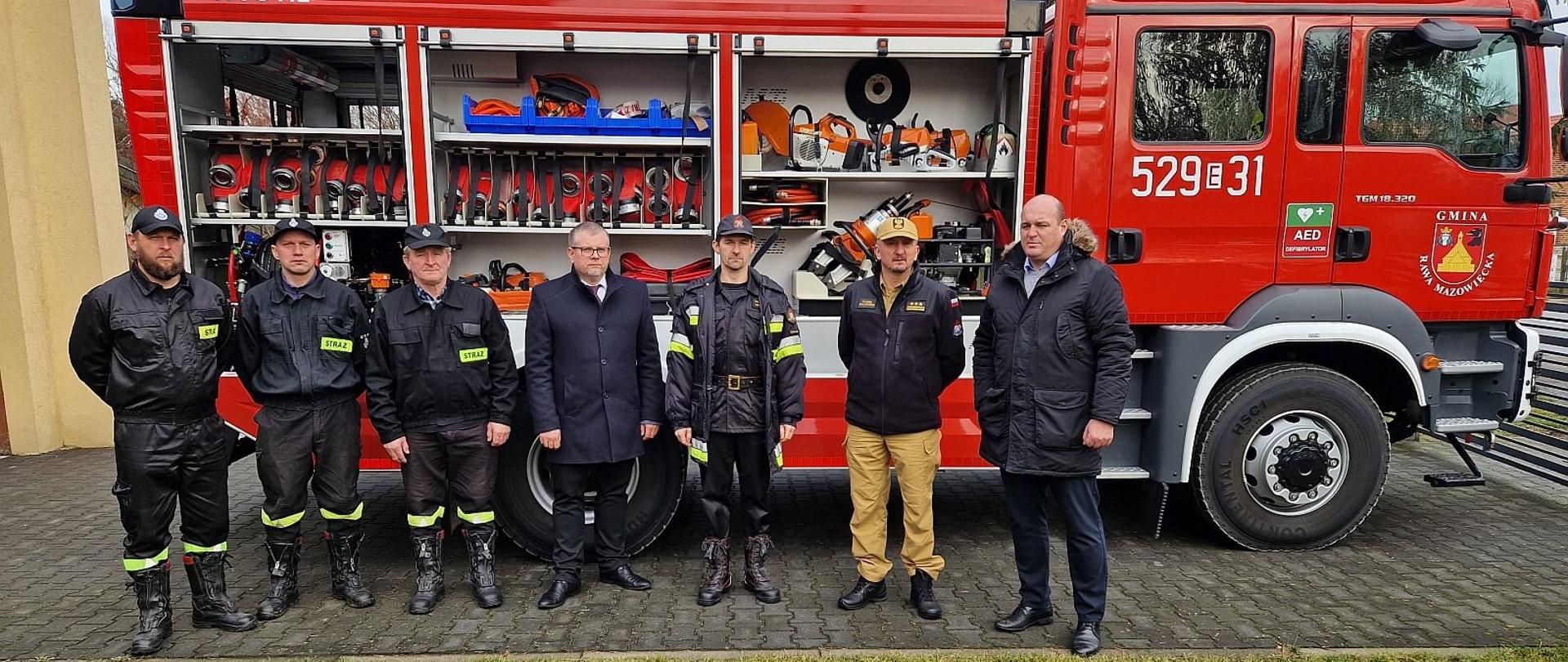 druhowie OSP, strażacy PSP oraz wójt gminy pozują do zdjęcia na tle samochodu gaśniczego