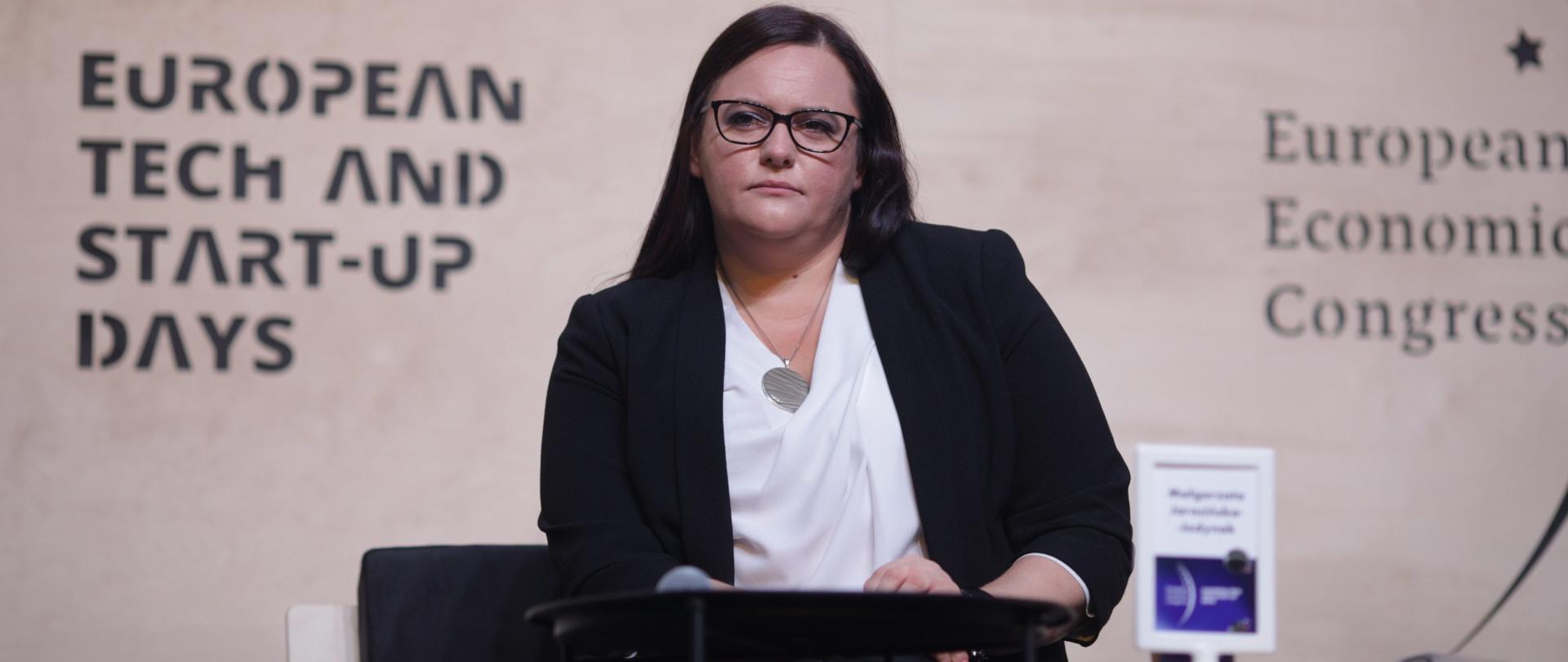 Minister Małgorzata Jarosińska-Jedynak siedzi przy stoliku. Za nią napis
European Tech and Start-up Days.