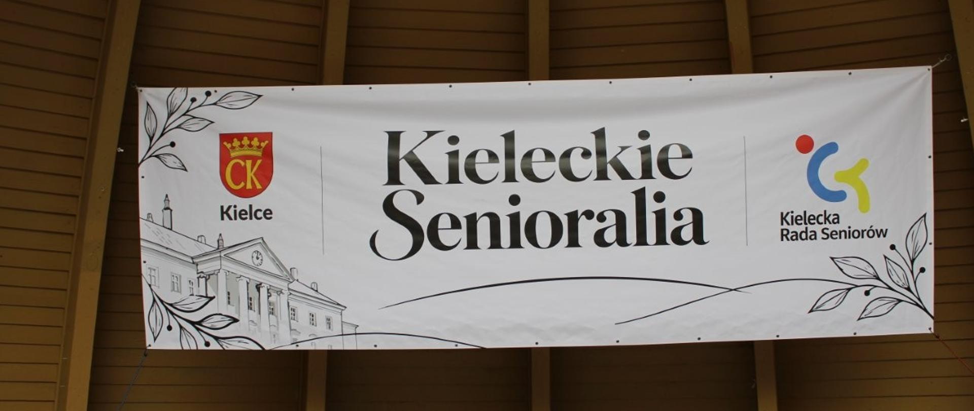 Baner z nazwą Kieleckie Senioralia zawieszony w muszli koncertowej Parku Miejskiego w Kielcach