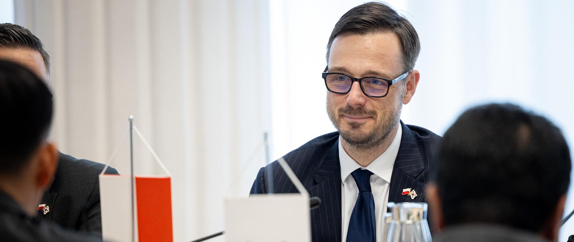 Minister Aktywów Państwowych podczas spotkania się z delegacją Korei siedzi przy stole.