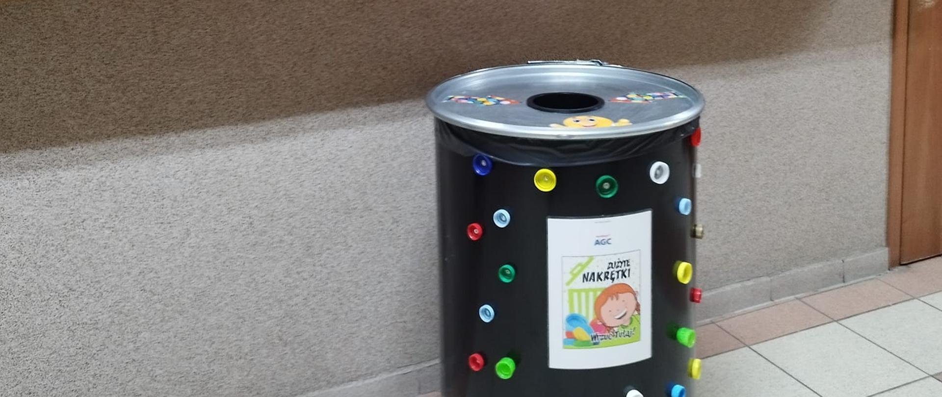 zdjęcie przedstawia beczkę (pojemnik) na zużyte nakrętki