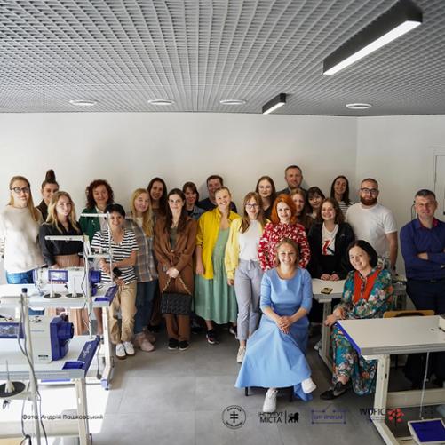 Kilkanaście osób pozuje do zdjęcia w zakładzie krawieckim.