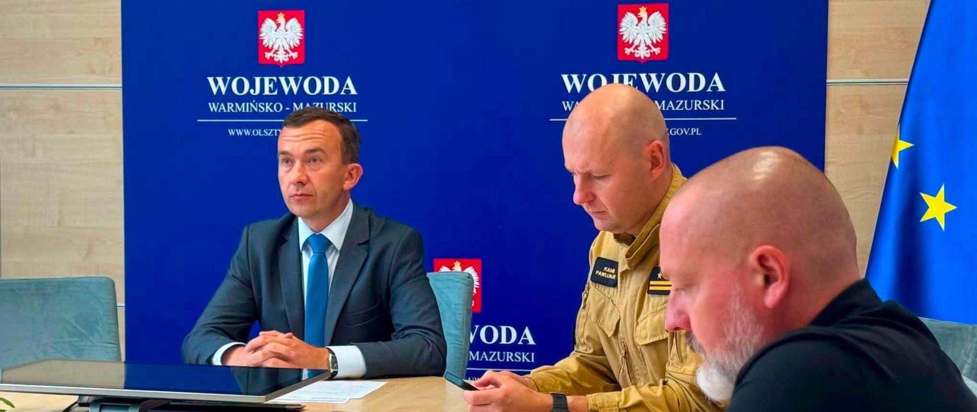3 mężczyzn, w tym wicewojewoda, siedzą przy stole konferencyjnym na tle ścianki wojewody