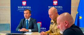 3 mężczyzn, w tym wicewojewoda, siedzą przy stole konferencyjnym na tle ścianki wojewody