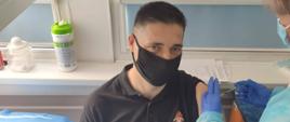 strażak w umundurowaniu dowódczo sztabowym w czarnym podkoszulku przyjmuje szczepionkę