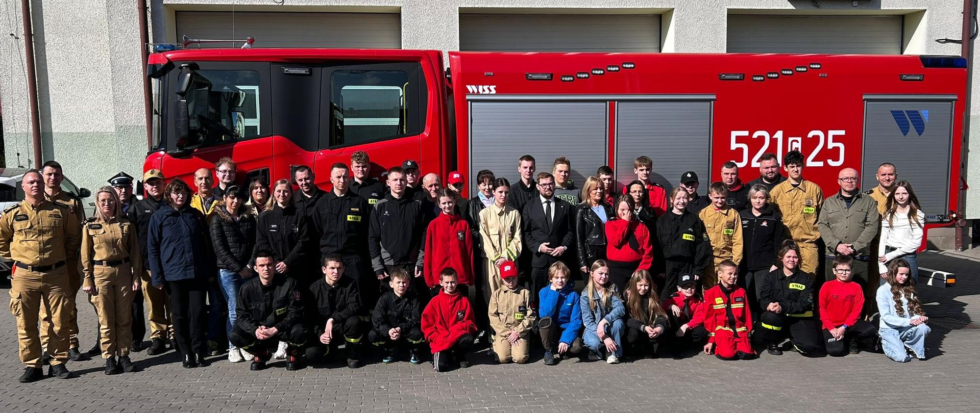 Pamiątkowe zdjęcie uczestników turnieju, opiekunów i prowadzących na tle samochodu pożarniczego