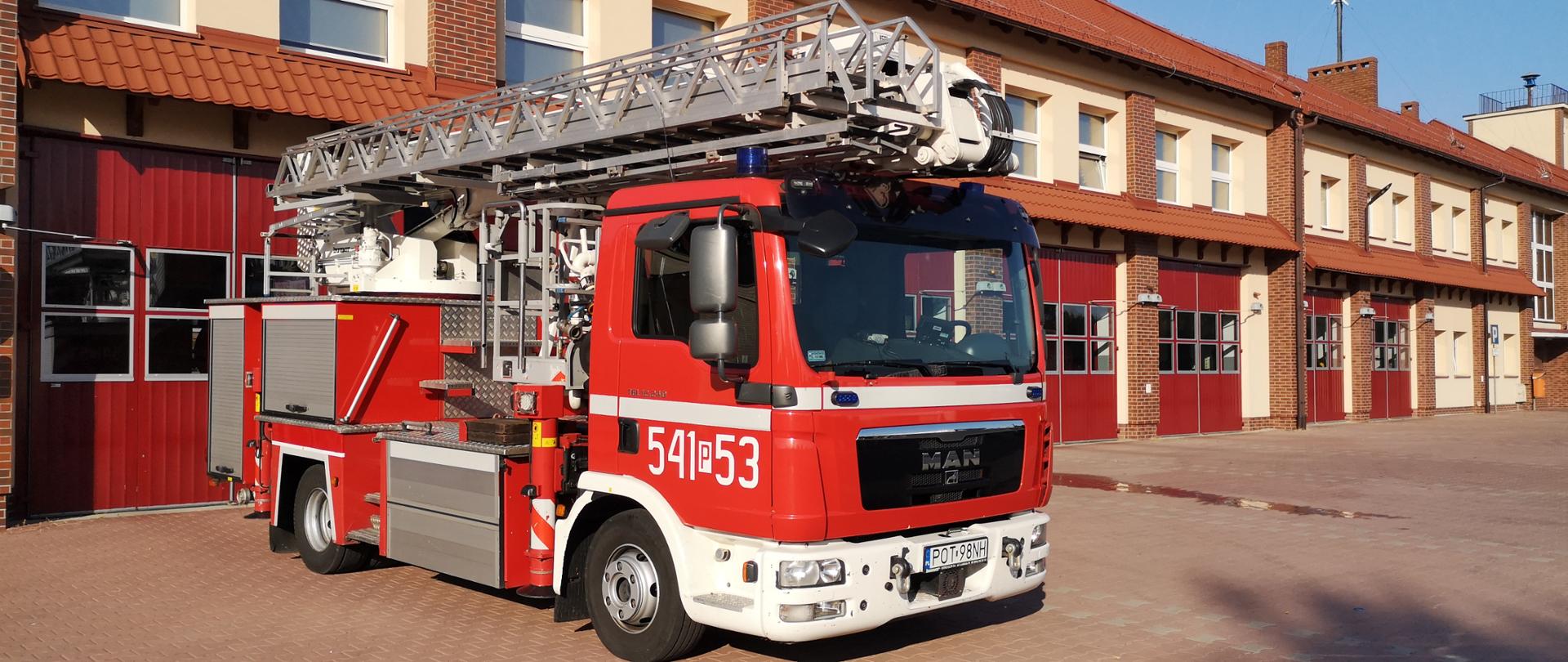Na zdjęciu samochód specjalny typu podnośnik hydrauliczny na placu manewrowym przed garażami Jednostki Ratowniczo-Gaśniczej