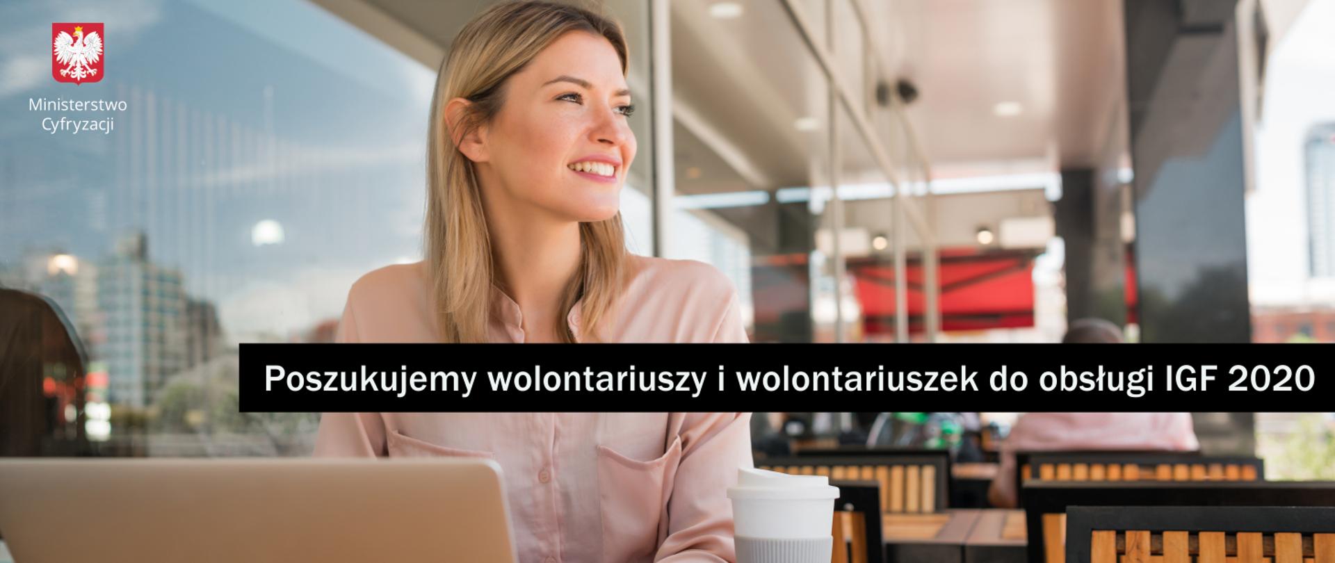 Zdjęcie przedstawia młodą siedzącą kobietę, pracującą przy laptopie. Obok laptopa stoi kubek z kawą