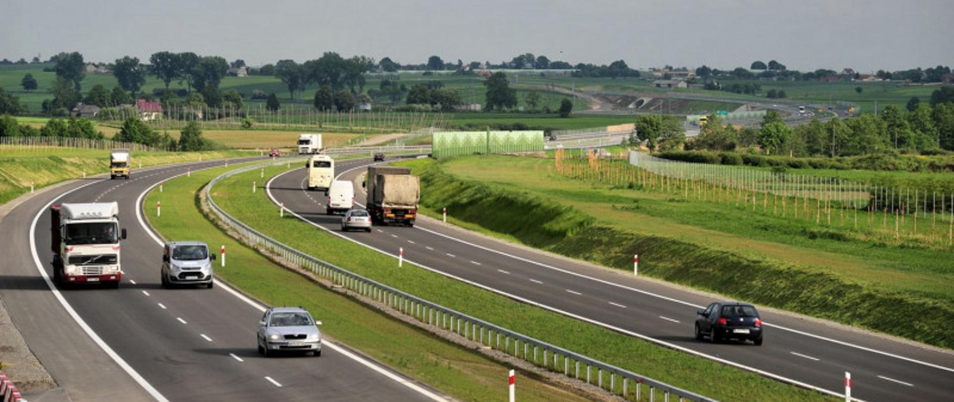Na zdjęciu widać samochody osobowe i ciężarówki jadące drogą ekspresową w obydwu kierunkach.