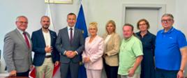 Grupa urzędników, samorządowców i przedstawicieli administracji, w tym wicewojewoda, stoi do wspólnego zdjęcia. W tle widoczne są flagi Polski i Unii Europejskiej oraz godło państwowe.
