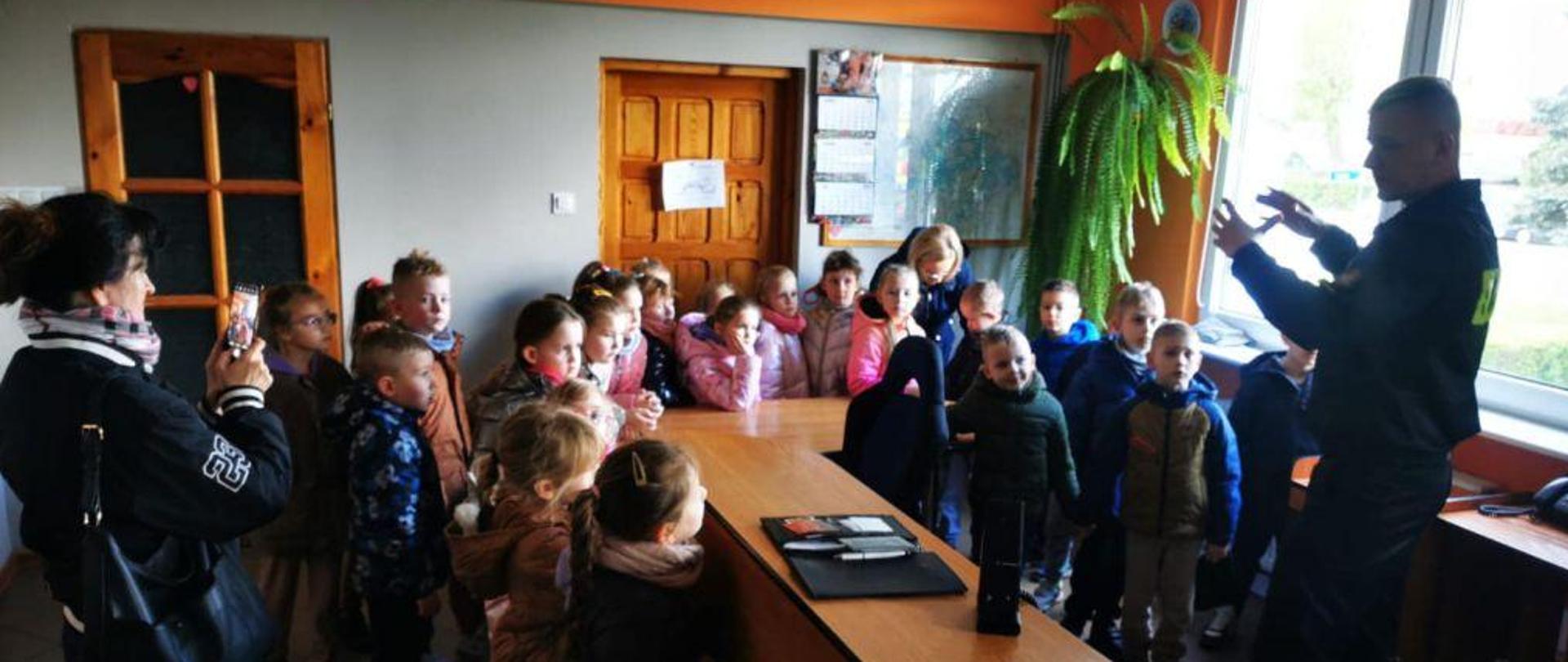 Dzieci stoją na stanowisku kierowania. Przy dzieciach strażak opowiadający o zgłaszaniu zdarzenia.