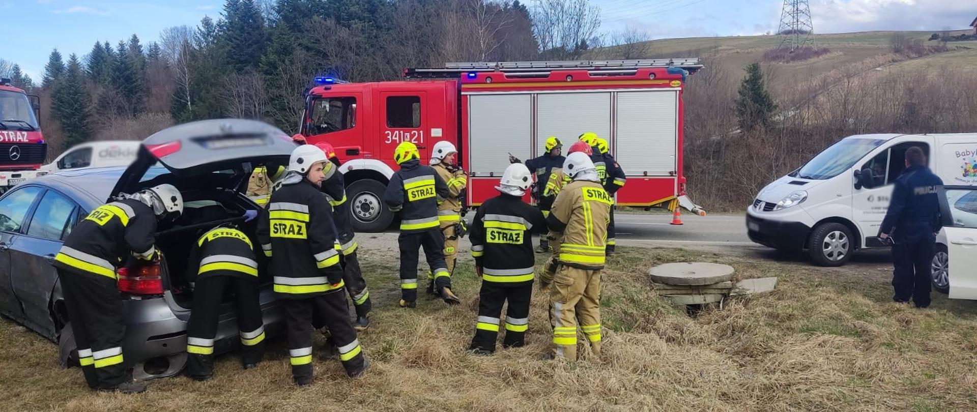 Strażacy przy samochodzie osobowym poza drogą prowadza działania 
