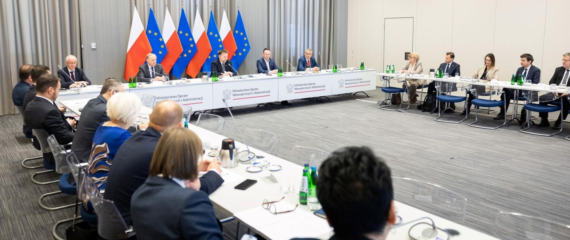 Grupa ludzi (minister spraw wewnętrznych i administracji, wiceministrowie i wojewodowie) siedzą przy stole podczas narady