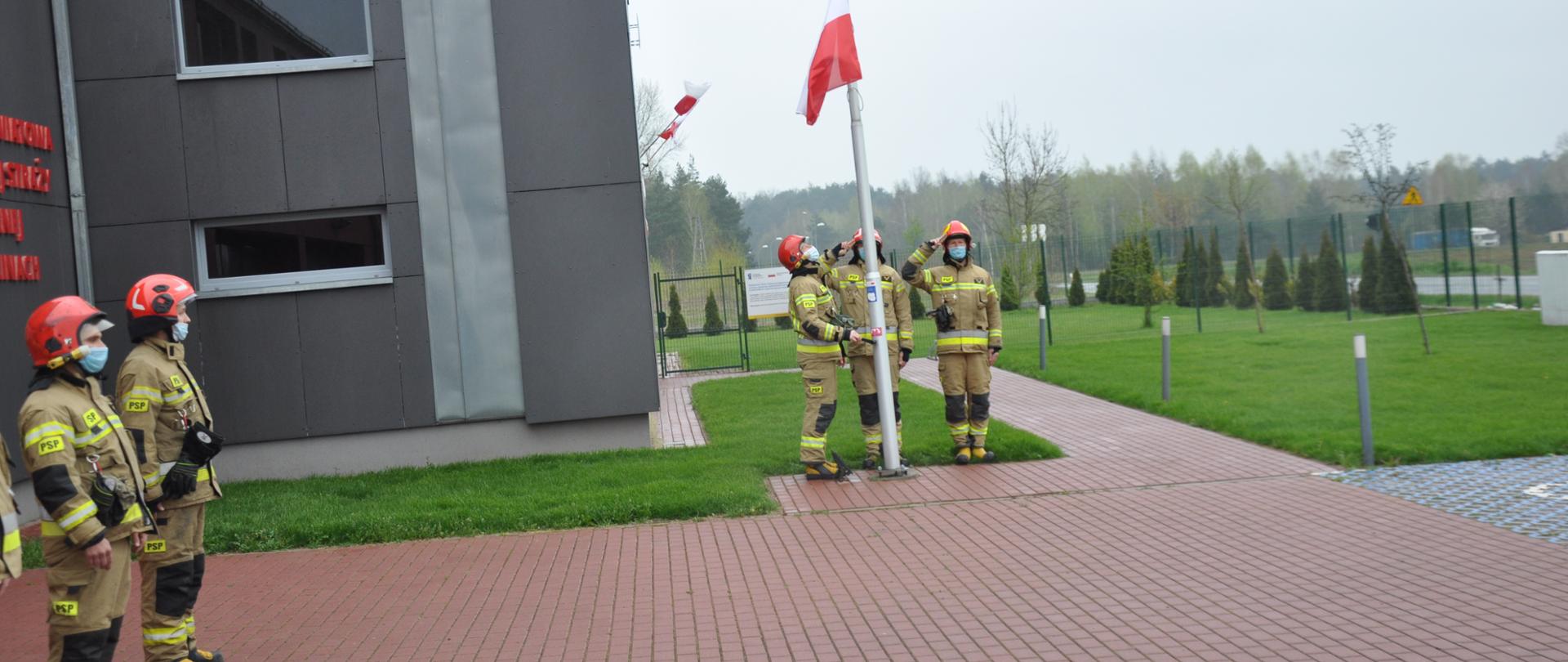 Na zdjęciu poczet flagowy - trójka strażaków podczas podniesienia flagi państwowej - wciąganie na maszt