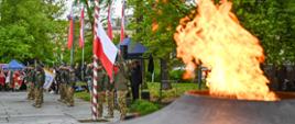 Plac Pamięci Narodowej w czasie uroczystości. Po prawej widoczny płomień z palącego się znicza, w głębi po lewej stojące na placu poczty sztandarowe