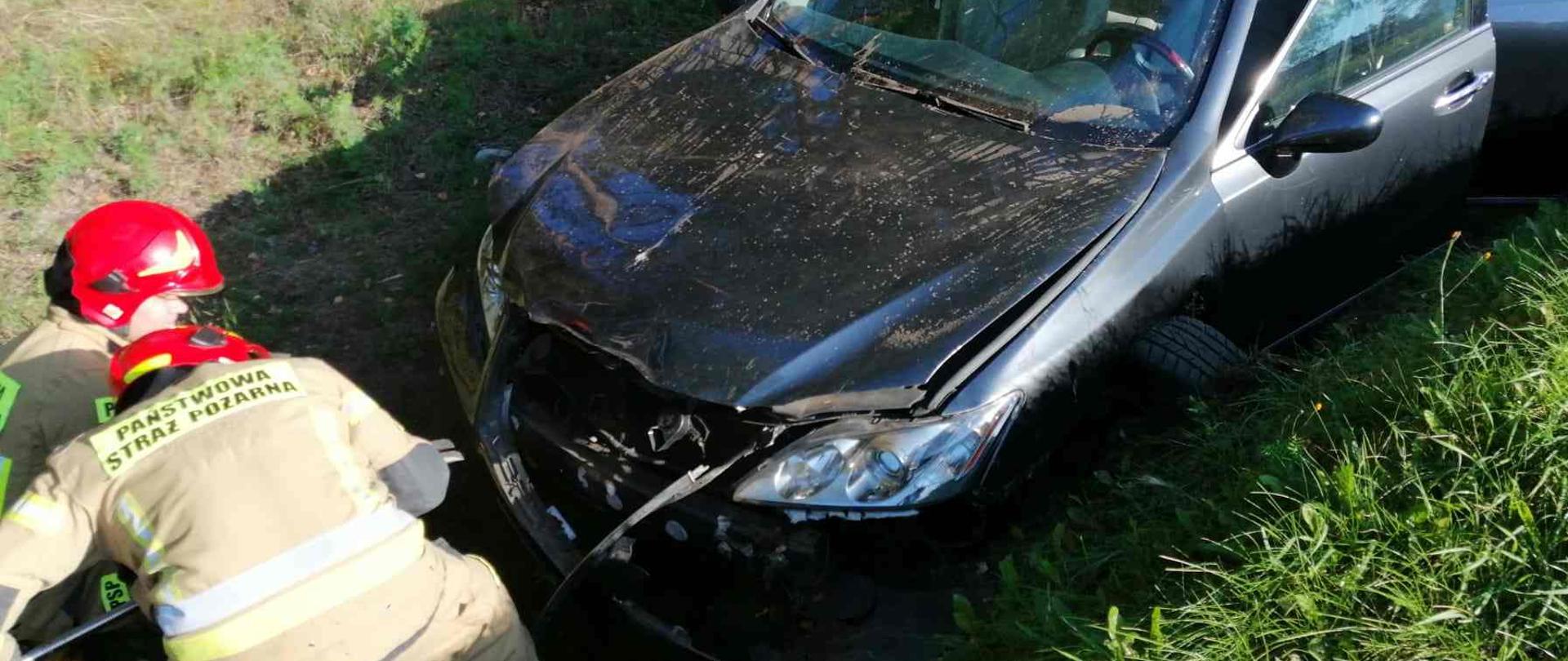 Strażacy usiłujący otworzyć maskę pojazdu.