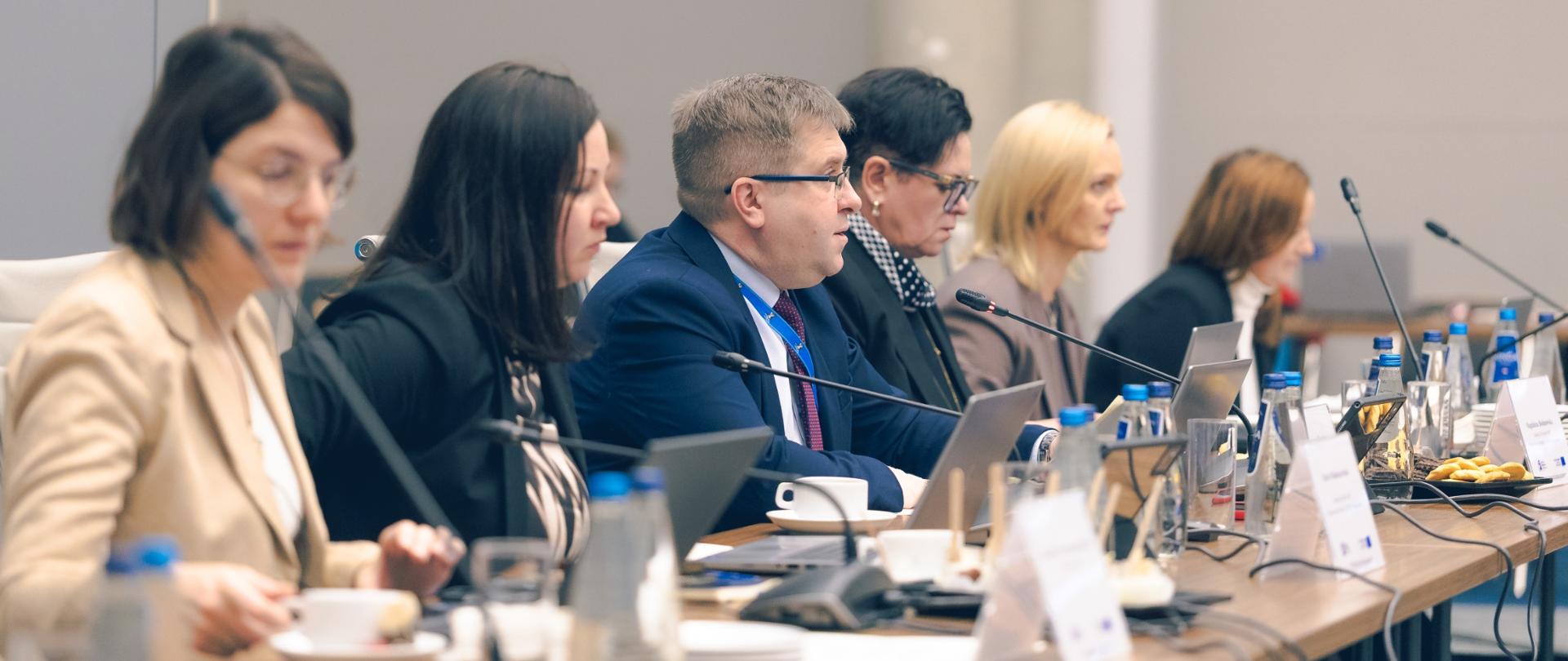 Na zadjęciu widać uczestników spotkania siedzących przy stole konferencyjnym