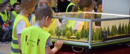 Dzieci patrzą na mobilny symulator zagrożeń pożarowych w postaci makiety lasu.