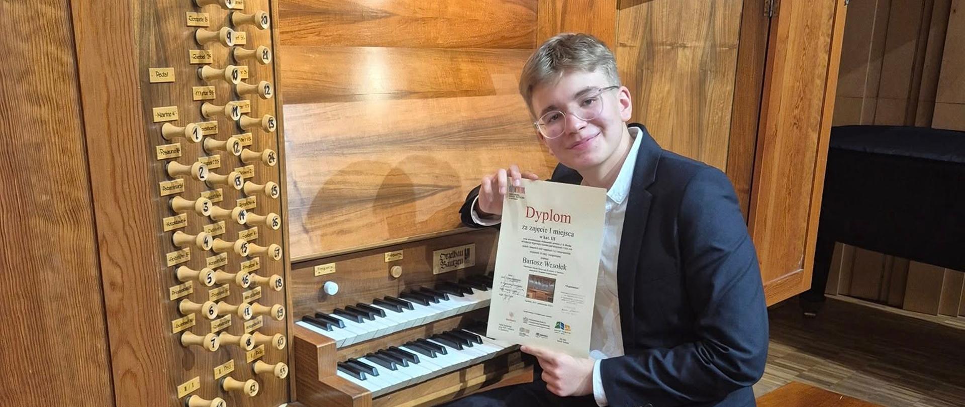 Bartosz Wesołek przy organach; w ręku trzyma dyplom za zajęcie I miejsca w Konkursie