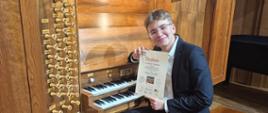 Bartosz Wesołek przy organach; w ręku trzyma dyplom za zajęcie I miejsca w Konkursie