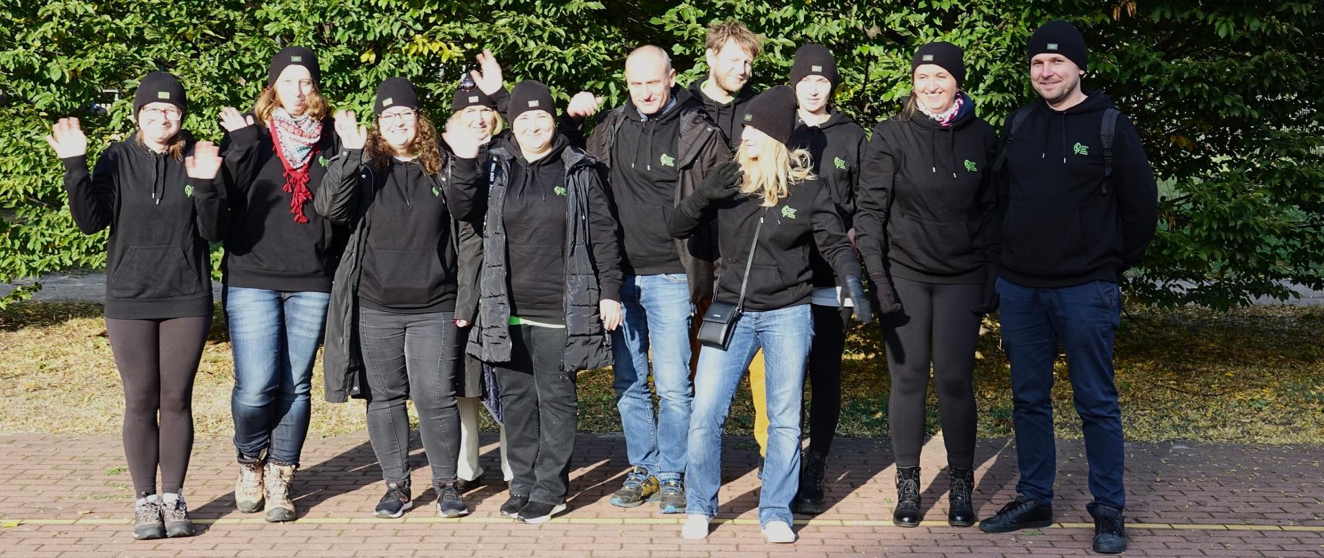 Grupa osób w czarnych bluzach ustawionych do zdjęcia grupowego na tle drzew