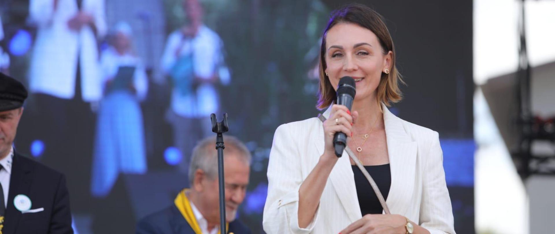 kobieta (wojewoda) stoi na scenie , w ręku trzyma mikrofon, za nia osoby w strojach kaszubskich 