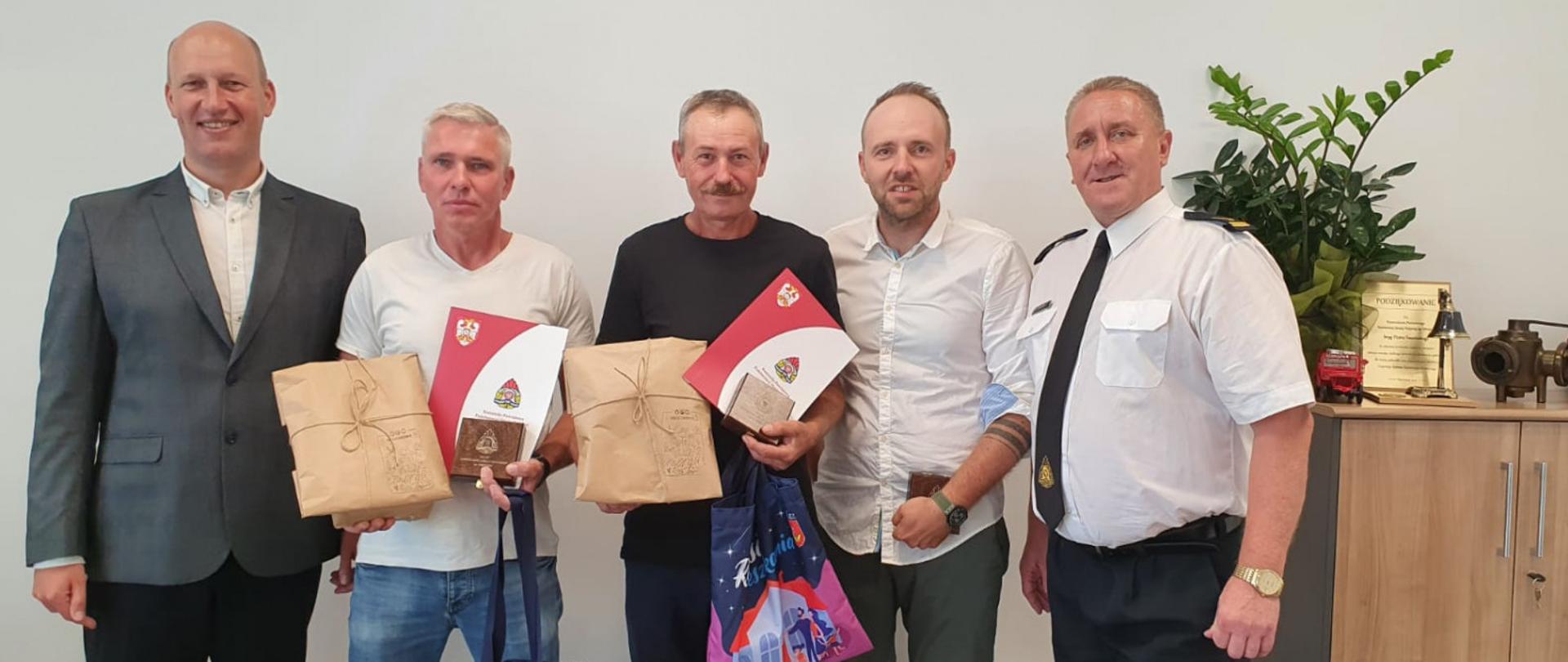 Na zdjęciu znajduje się pięciu mężczyzn. Dwóch z nich z wręczonymi upominkami. 