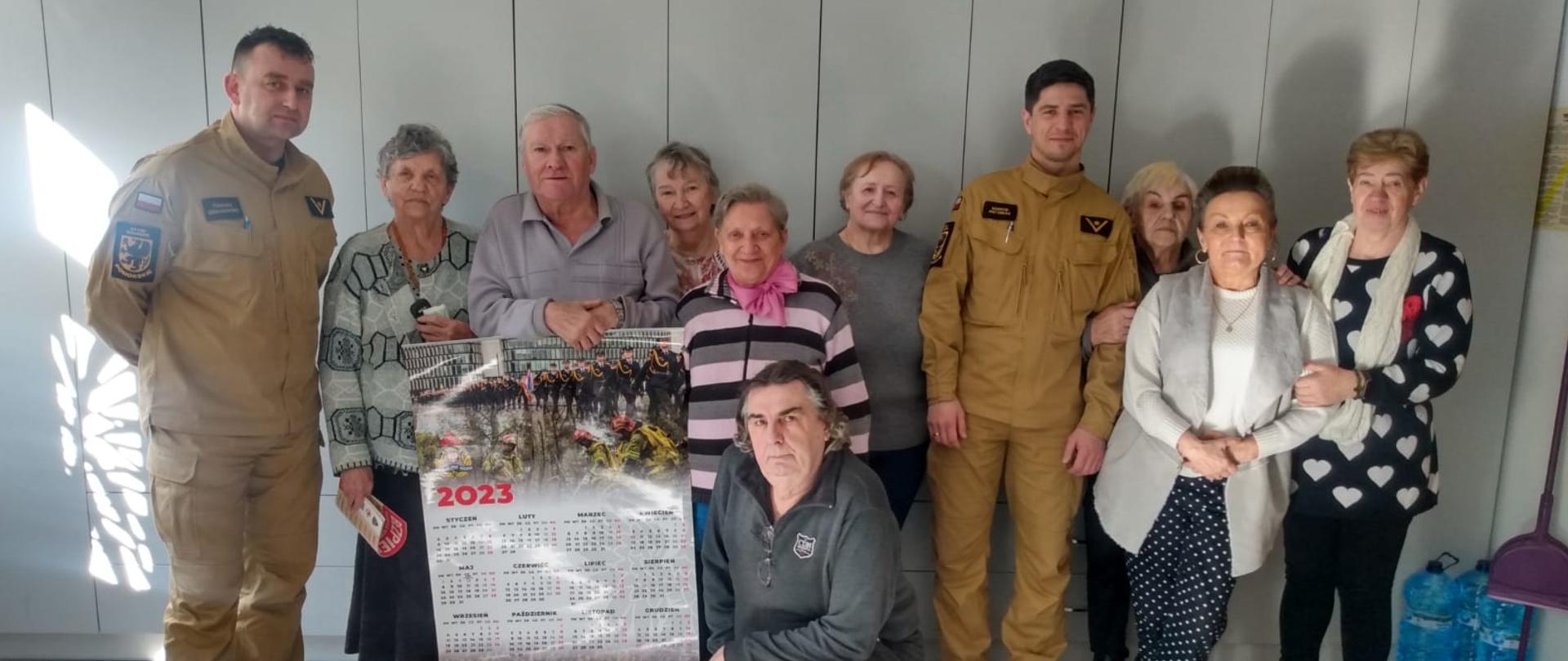 Fotografia przedstawia strażaków wraz z seniorami na zdjęciu grupowym