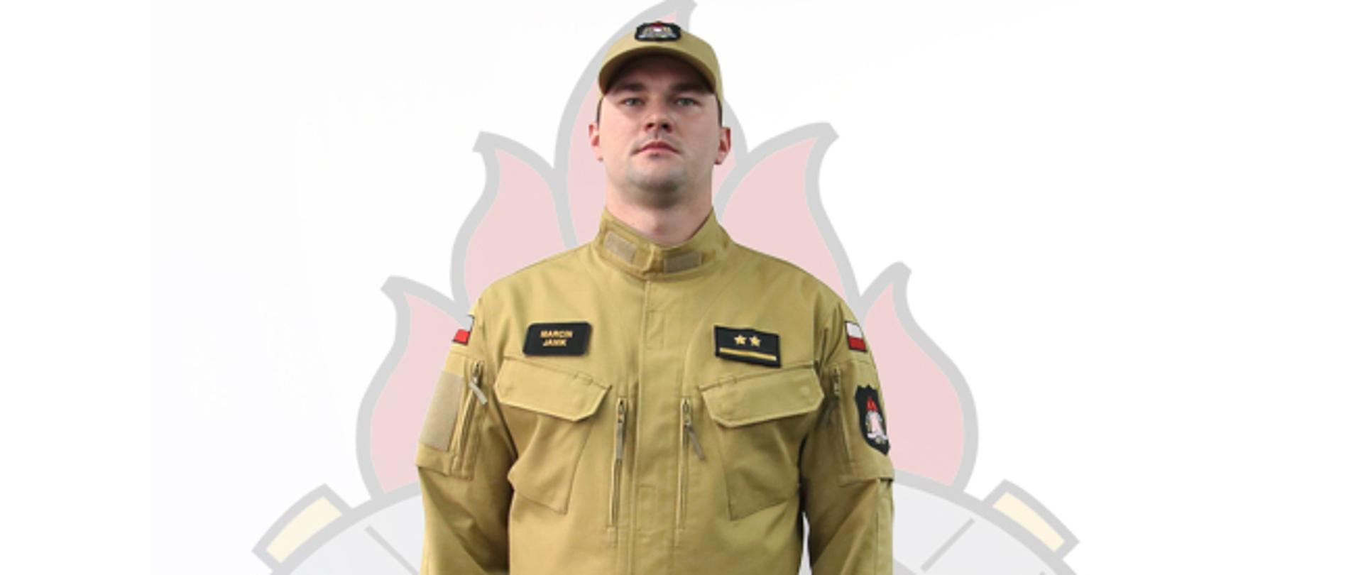 Fotografia przedstawia mężczyznę, który jest odwrócony przodem do obiektywu. Ma na sobie beżową bluzę, beżowe spodnie, czarne buty i beżową czapkę z daszkiem.