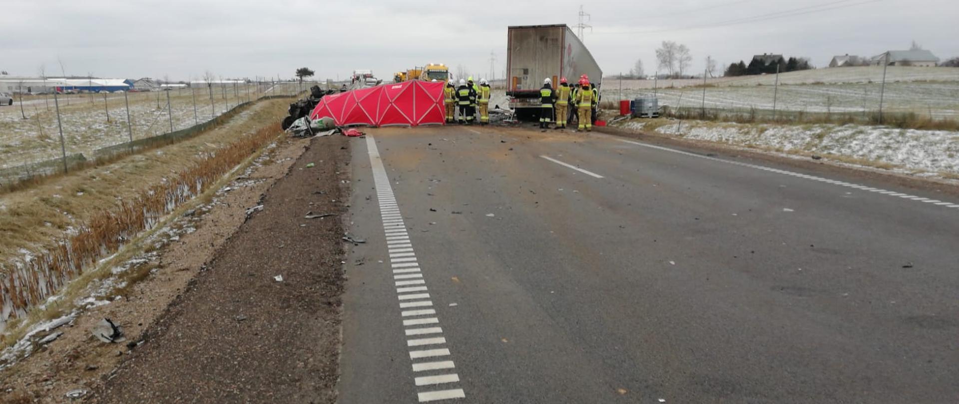Na zdjęciu widoczny jest wrak samochodu ciężarowego, osobowego oraz strażaków podczas działań ratowniczo gaśniczych.