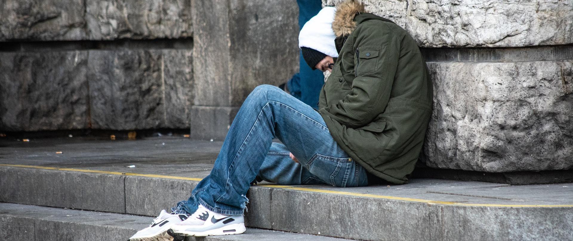 Młody mężczyzna skulony pod ścianą budynku