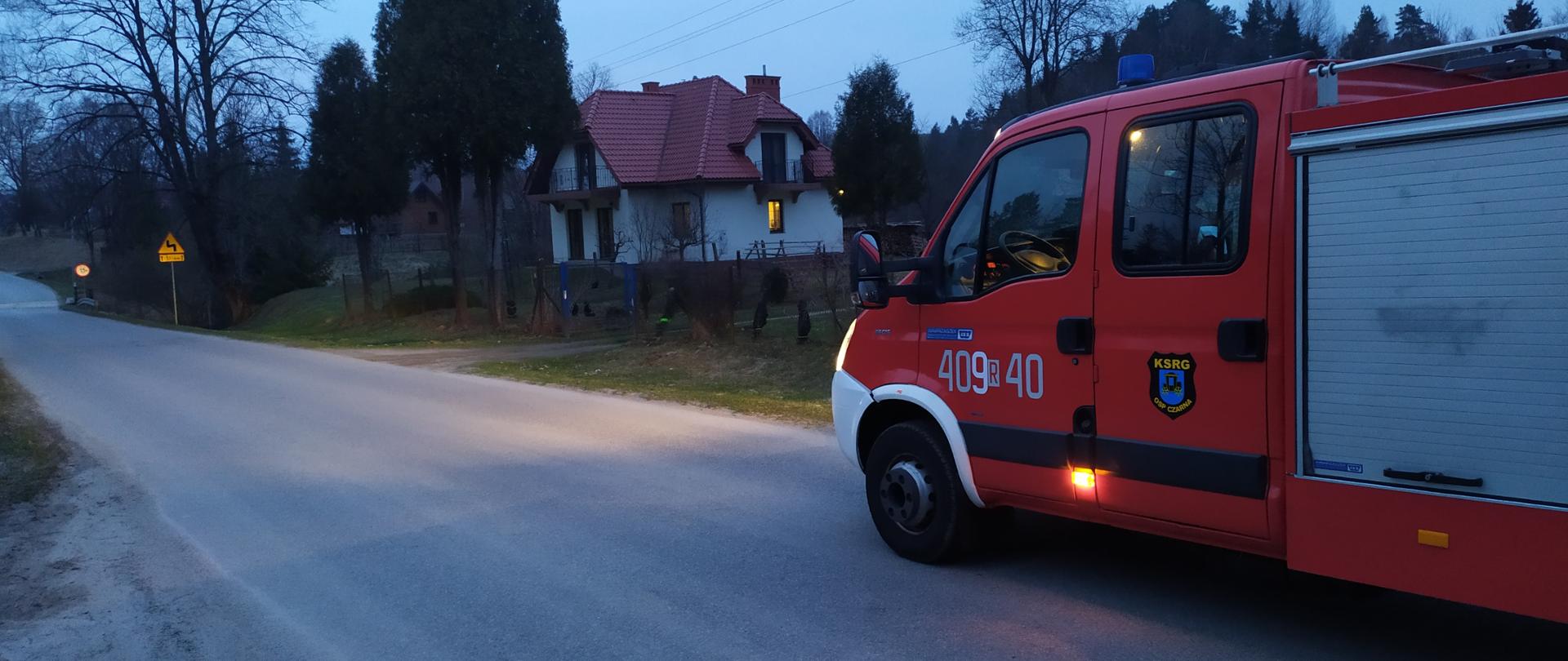 Na zdjęciu samochód pożarniczy na drodze w tle dom i drzewa