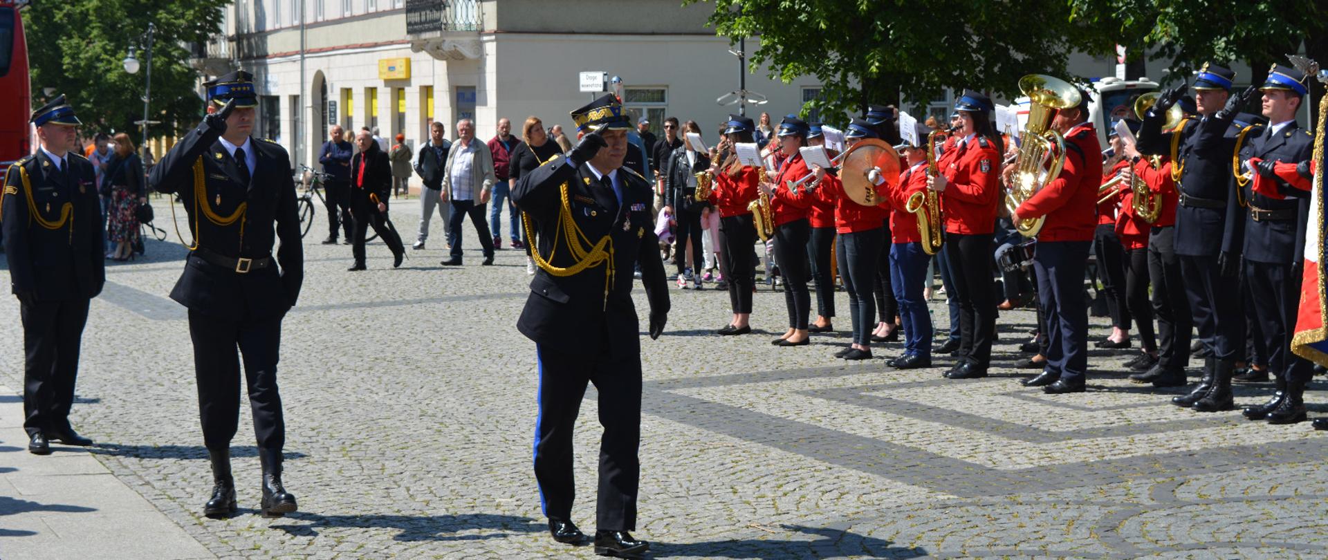 Zdjęcie wykonane w centrum miasta Radomia, na ulicy Żeromskiego w pobliżu Placu Corazziego. Na zdjęciu widać Mazowieckiego Komendanta Wojewódzkiego Państwowej Straży Pożarnej w Warszawie nadbrygadiera Jarosława Nowosielskiego, który w asyście dowódcy uroczystości dokonuje przeglądu pododdziałów biorących udział w obchodach Dnia Strażaka. Funkcjonariusze ubrani są w mundury galowe. 