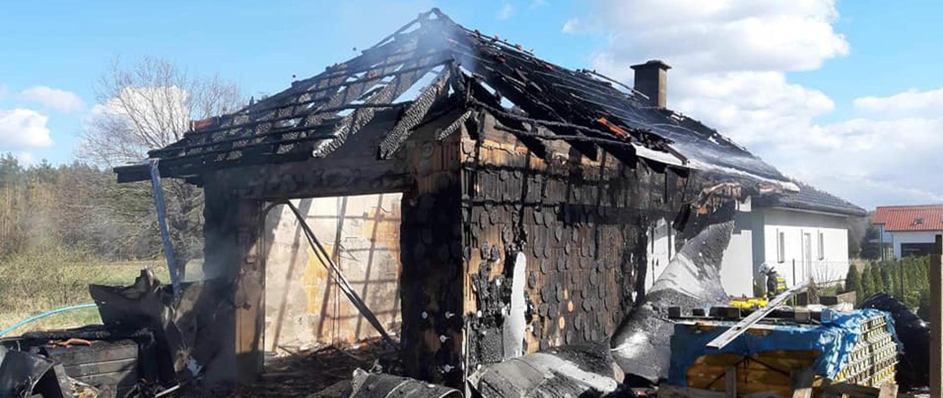 Widoczny spalony budynek garażu wolnostojącego. Wokół leżą spalone elementy budowlane.
