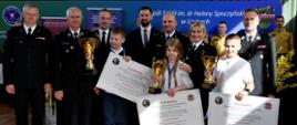Wspólne zdjęcie laureatów turnieju z funkcjonariuszami PSP. Laureaci trzymają w rękach puchary i nagrody. 