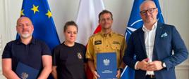 4 osoby pozują na tle flag UE, Polski oraz NATO