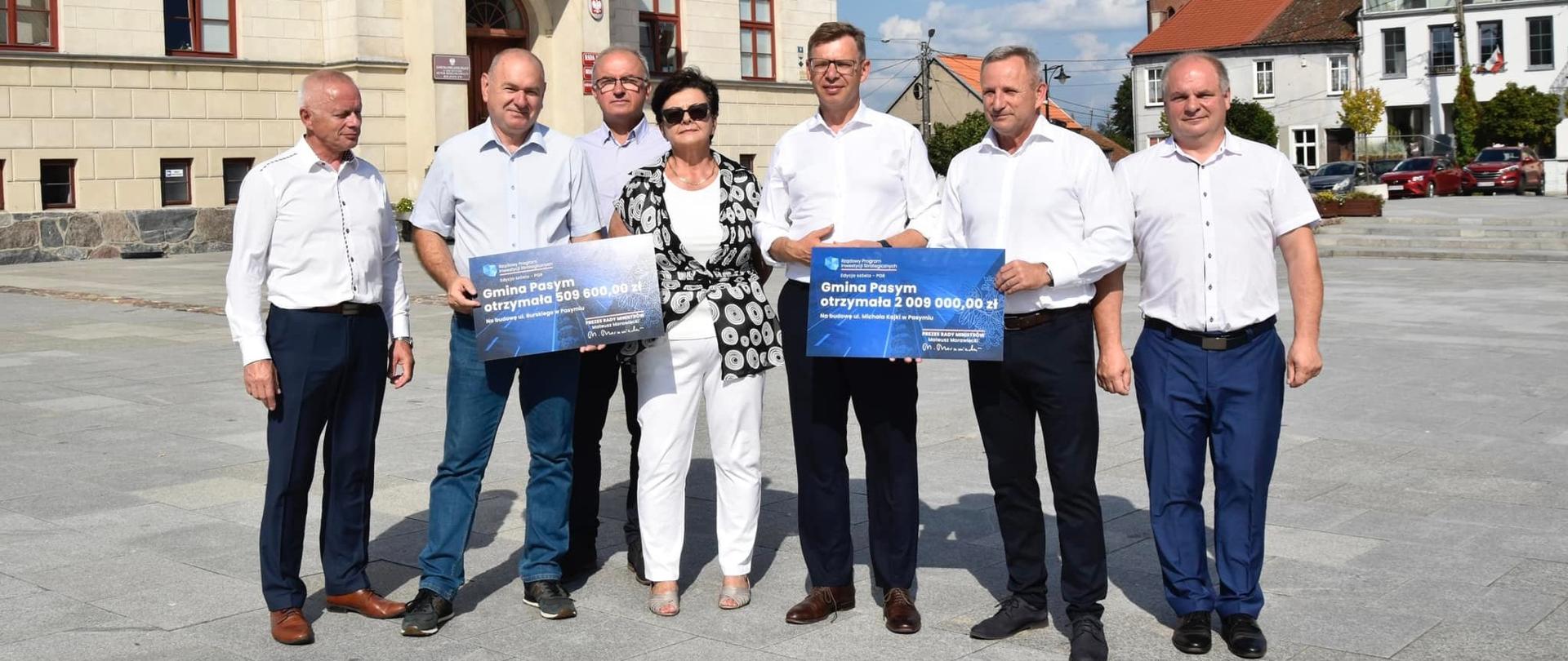 Wojewoda Artur Chojecki oraz Burmistrz Pasymia Cezary Łachmański wraz z innymi osobami stoją przed ratuszem w Pasymiu 