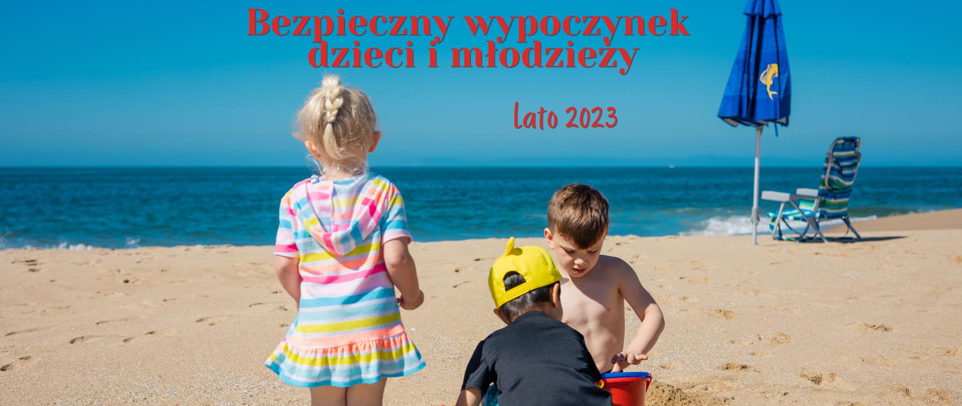 Trójka dzieci na plaży, od lewej dziewczynka, po prawej dwaj chłopcy bawią się w piasku, po prawej lezak i parasol