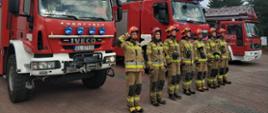 siedmiu strażaków ubranych w stroje specjalne stoi na tle trzech czerwonych samochodów ratowniczo gaśniczych za nimi znajduje się budynek PSP w Łowiczu
