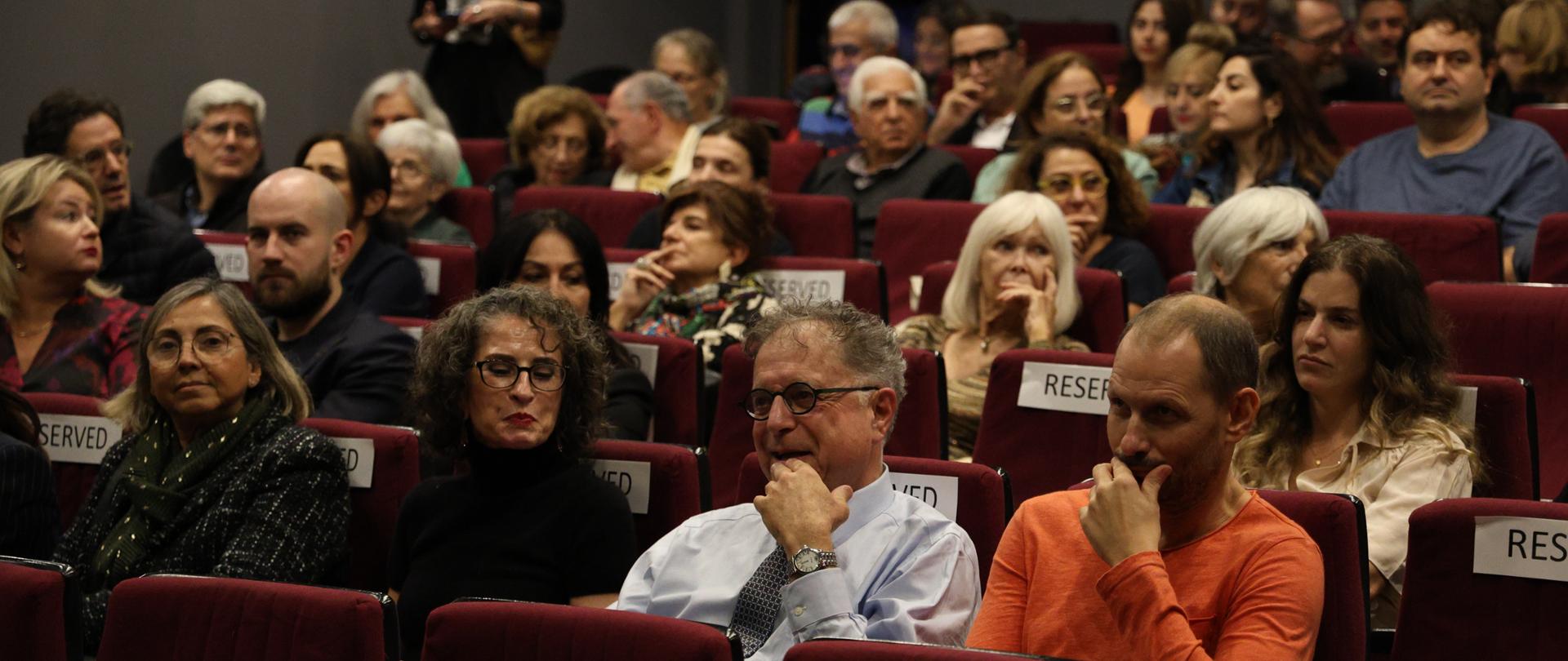 Tłum ludzi siedzi na fotelach kinowych czekając na projekcję filmu