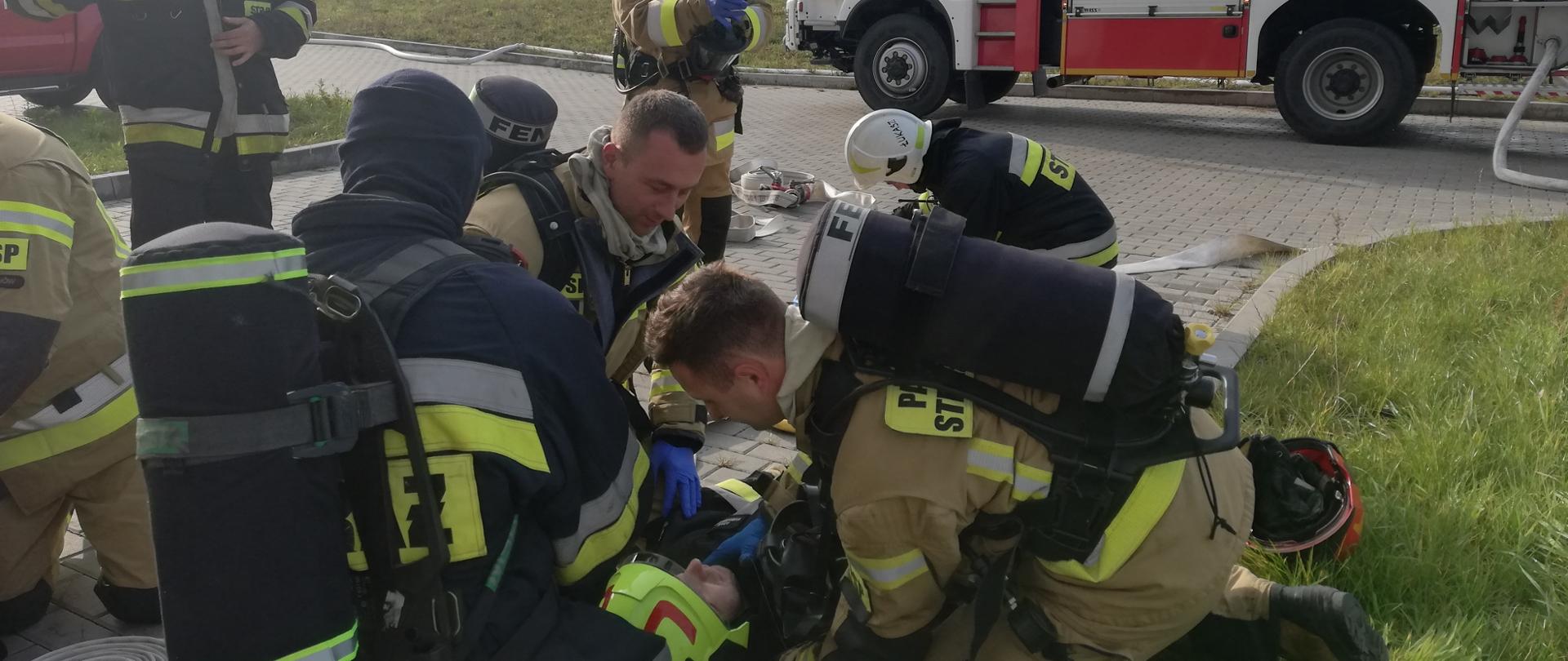 Przed zakładem Partner Systems strażacy udzielają kwalifikowanej pierwszej pomocy poszkodowanemu w trakcie działań (ćwiczeń) funkcjonariuszowi.