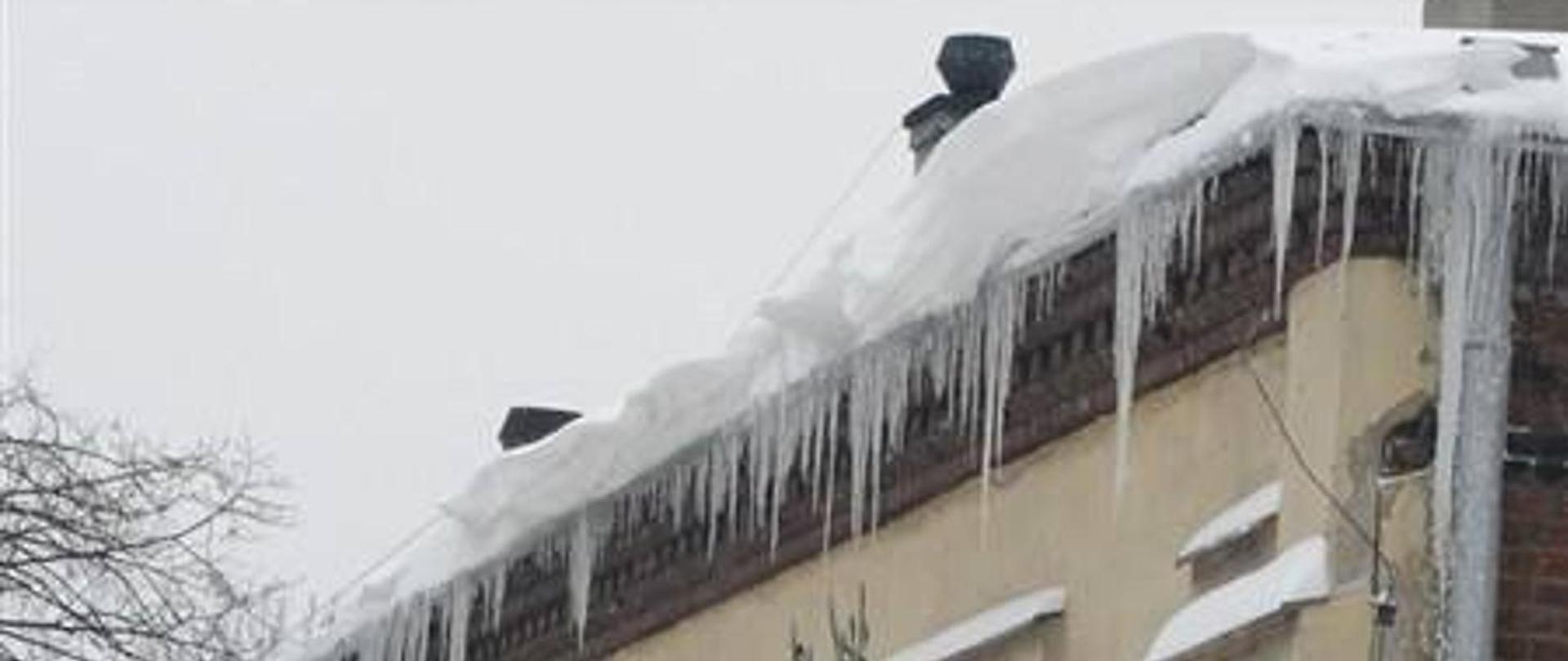 Zdjęcie obrazuje śnieg i sople na dachu budynku